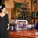 エリザベス女王はテーブルの後ろに座っており、王室の4人の額入り写真がテーブルに置かれています。